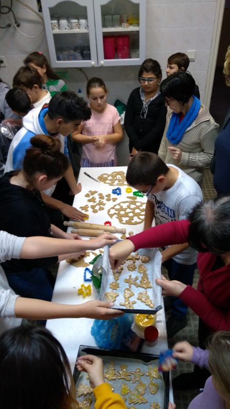Adventi kézművesség - Karácsonyi köszöntő A képen gyerekek mézeskalácsot készítenek egy asztal körül.